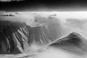 Black and white high snowy mountains covered with beautiful clouds and fog in snowfall