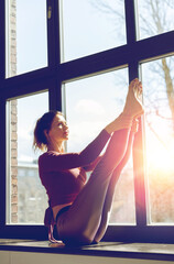 Fototapeta na wymiar fitness, sport and healthy lifestyle concept - woman doing yoga exercise on window sill at studio