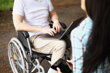 Fototapeta na wymiar Man in wheelchair works on laptop on street next to woman sits and holds tablet
