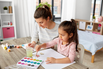 Obraz premium family, motherhood and leisure concept - mother spending time with her little daughter with colors painting chipboard items at home