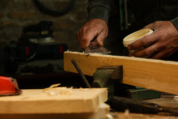 Handyman is smoothing wooden plank with skim coat. Applaying putty on a piece of wood.