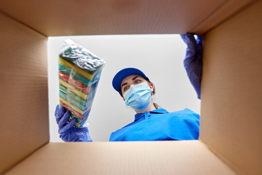 Home Delivery, Shipping And Pandemic Concept - Woman In Protective Medical Mask And Gloves Packing Parcel Box With Dish Washing Sponges