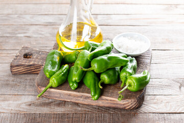Fresh green pimientos or padron peppers, sea salt, olive oil on a wooden table. Spanish cuisine. Pimientos de Padron.