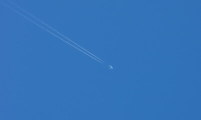 plane in the sky with two diagonal con  trails against blue sky