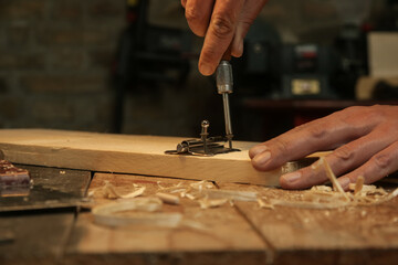 Carpenter screwing metal chrome hinges on wooden plank in the workshop.
