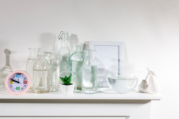 A set of water bottles of different shapes with a photo frame and a pot with artificial succulent is on the dresser