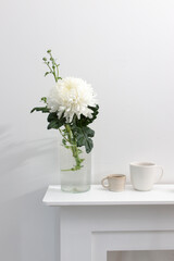 A large chrysanthemum in a glass vase, two fluted cups of coffee and ceramic bird figurines on the table. Office decoration.