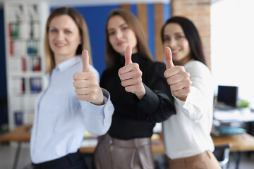 Three businesswoman smiling and holding thumbs up in office