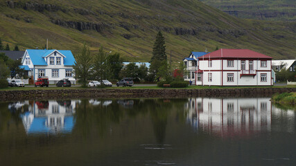 Fototapeta na wymiar Colorful traditional buildings and houses in the green nature on the picturesque fjord, reflect in the sea water, Seydisfjordur, Iceland
