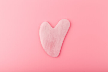 Top view of pink heart shaped guasha stone made of quartz crystal on bright pink background....