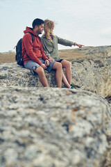 Couple sits on a rock, looking at the landscape and enjoying the view and fresh air.