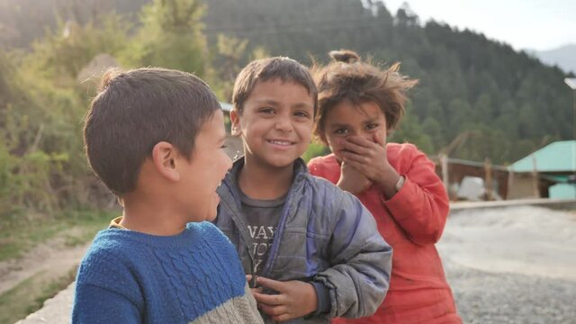 Close up daylight outdoor shot of a group of happy cute young little rural kids looking at the camera and laughing against the village background
