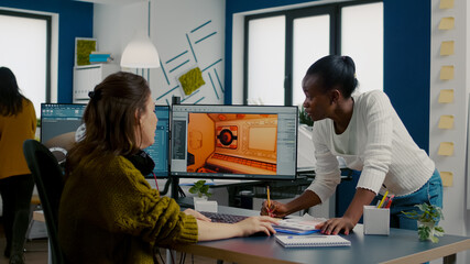 Multiethnic women game designer looking at computer with dual displays working together at project in studio office. Gamer workers developing new online video games on pc with modern technology