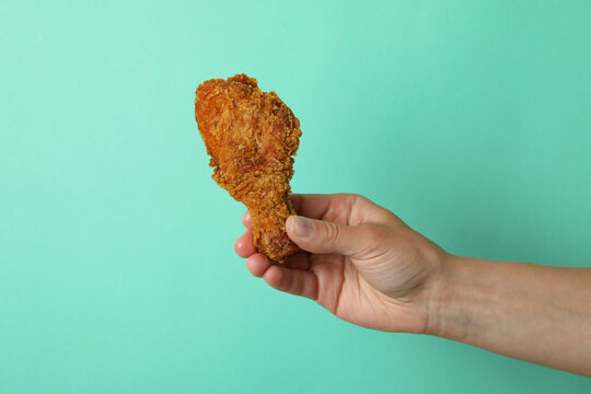Female hand holds fried chicken on mint background