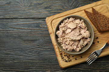 Board with plate of canned tuna on wooden background