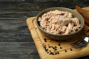 Board with plate of canned tuna on wooden background