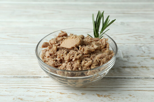 Bowl with canned tuna on white wooden background