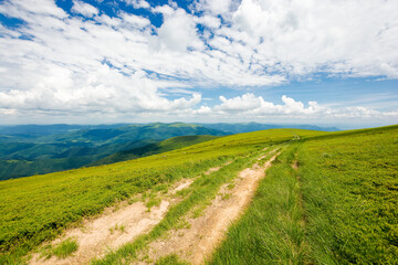wide trail through grassy meadow. mountain ridge in the distance beneath a gorgeous cloudscape on the blue sky. travel backcountry concept