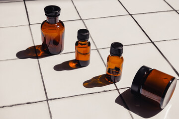 Creative composition of brown glass cosmetic bottles for oil, serum and beauty products standing in a row on a white tile bathroom background with sharp shadows on a sunny day. Advertising mock up.