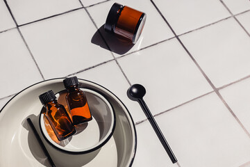 Creative flat lay composition of natural eco-friendly cosmetic products in brown glass bottles and accessories on a white bathroom tile countertop background. Beauty routine.