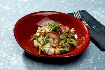 Appetizing salad with eel, teriyaki sauce, lettuce in a red plate on a blue background