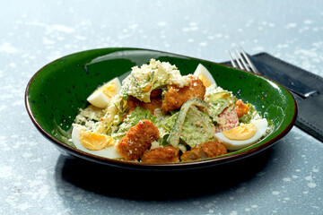 Appetizing salad with chicken breaded and deep fried, parmesan, egg, lettuce and white sauce in a green plate on a blue background