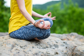 woman meditating in lotus pose on a rock in summer