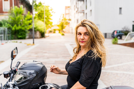 portrait of blonde mature woman with biker helmet sitting on motorcycle outdoors