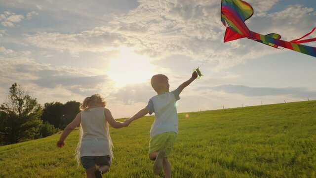Little children running holding hands playing with a kite in the meadow