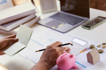Business owner checking saving account passbook and using a calculator with money coin, piggy bank,...