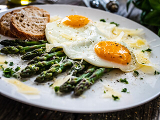 Tasty breakfast. Sunny side up eggs with green asparagus and parmesan served on black plate on wooden table
