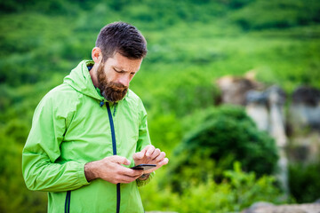 Naklejka na ściany i meble man trekking checking map on smartphone in summer scenery