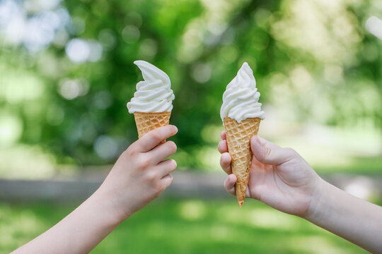 Two cones with creamy ice cream in children's hands. Children walk in the park in summer and eat sweets. Horizontal photo with place for text.