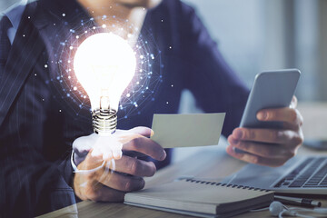 Double exposure of man's hands holding and using a digital device and bulb hologram drawing. Idea concept.
