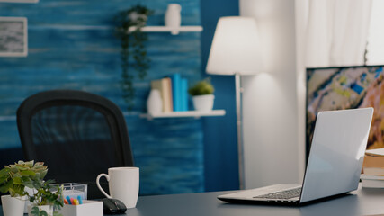 Empty workplace home office with modern design and laptop placed on desk. Living room with nobody...
