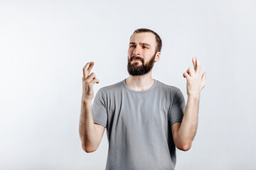 Naklejka premium Handsome young man frown and cross fingers in hope on white background with space for advertising mock up