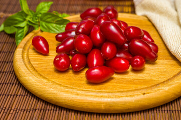 Still life - fresh large dogwood berries, purple plums and a sprig of basil on a wooden board
