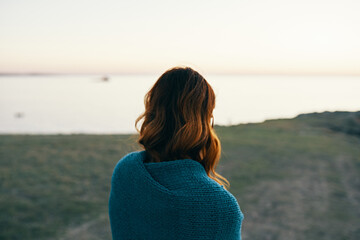 red-haired woman in the mountains with a blue plaid on her shoulders back view