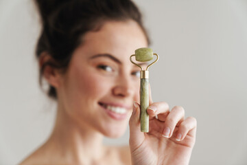 Half-naked brunette woman smiling while showing jade roller © Drobot Dean
