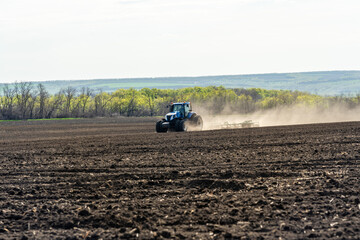 Obraz premium A blue tractor works on a field on a spring morning.