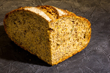 Slice of rustic natural yeast-free bread with flax, poppy seeds, sesame seeds, millet, pumpkin and sunflower seeds, on a black background, hard light, photo in a low key.