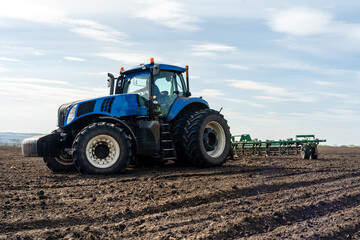 Fototapeta premium A tractor with seedbed cultivator ploughs field on morning.