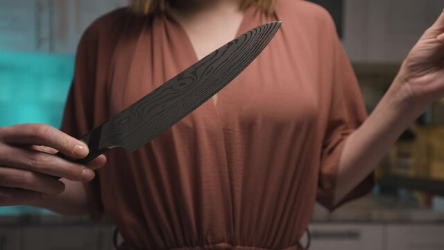 Close up of woman hands taking off a plastic tip from a steel knife at the kitchen at home. Action. Female holding a new sharp polished steel knife, concept of cooking.