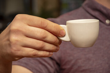 A man's hand holds a small white coffee cup.