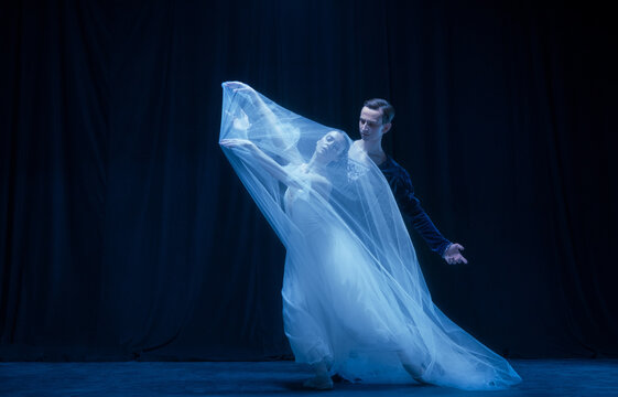 Graceful balerina in image of ghost bride with patner in art ballet performance isolated over dark background.