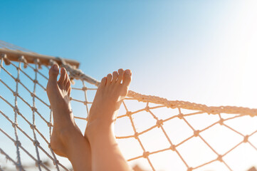view of woman relaxing on hammock. Low angle view. Beautiful female feet relaxing in a hammock on the beach against the background of the sky. horizontal is place for your text