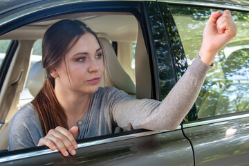 Young beautiful caucasian woman shaking with fist from the car. Agression during driving. Copy...