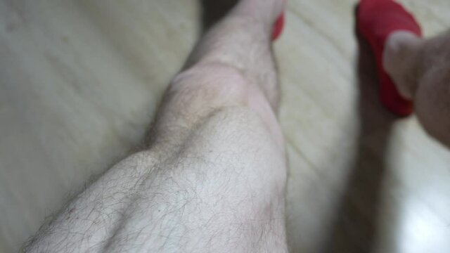 Young man works out at home. Soft focused footage. Swings the musculus of the feet or leg. Sport training in room. Close up, 4k.
