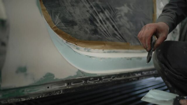 Repairing a car after an accident in a workshop garage. Cover the back of the body with white spackling paste. Professional auto Renovation.