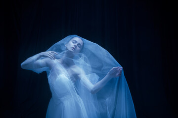 Despair. Young graceful balerina in image of ghost bride in art performance isolated on dark background in neon light. © Lustre Art Group 